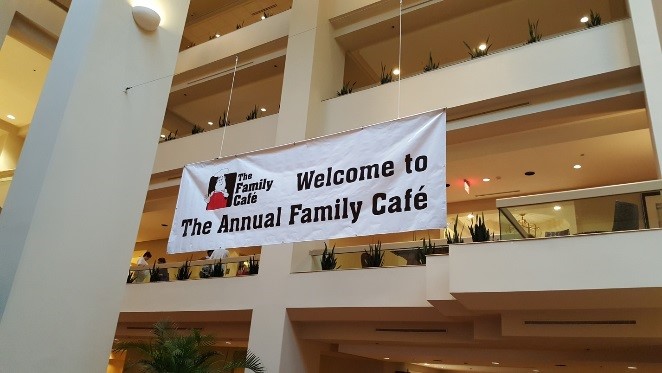 A banner hangs from inside a multiple-story building that has a man in a chef's hat (the Family Cafe logo) and the words "Welcome to the Annual Family Cafe"")