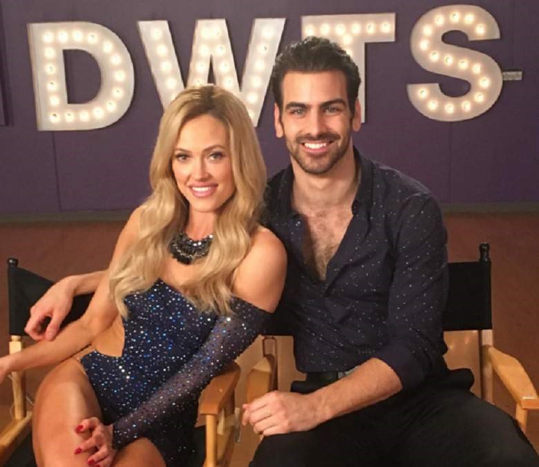 Nyle DiMarco and Peta Murgatroyd from Dancing with the stars Season 22 sit next to each other and smile in front of lit up letters "DWTS"