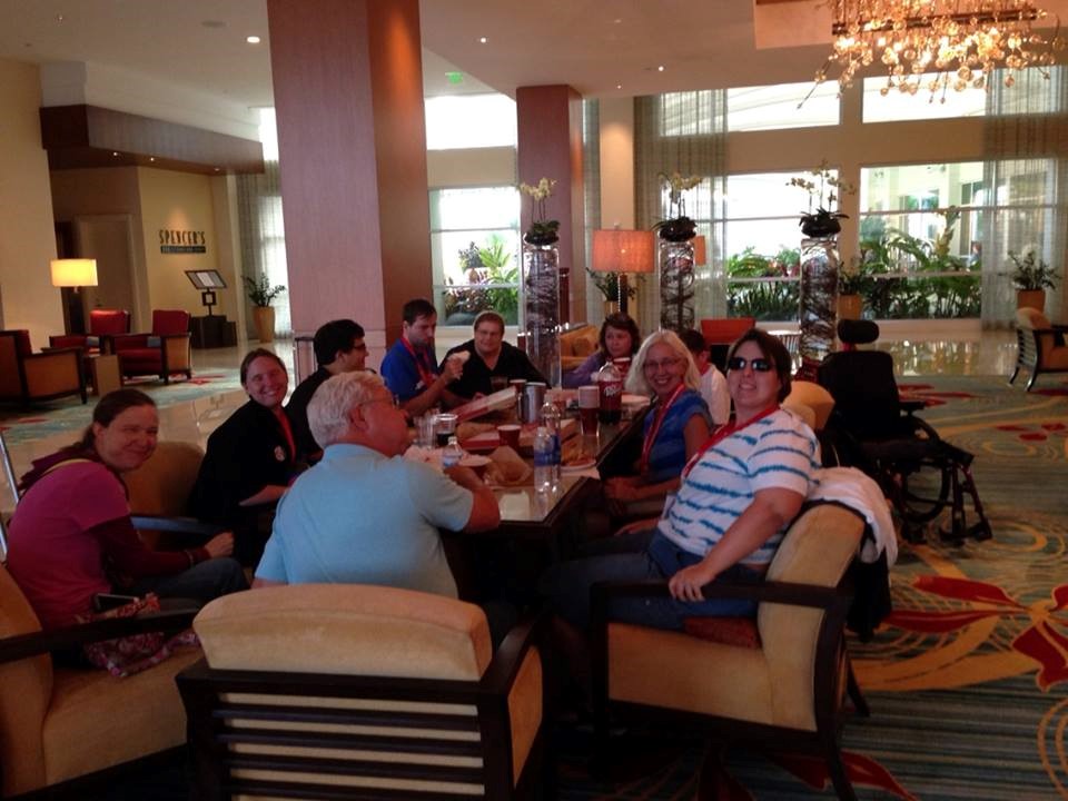 A group of 10 people sit around a large table and most of them smile at the camera.