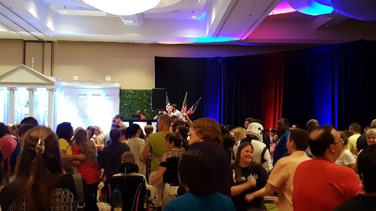 A crowded room of people, in the background is a structure that resembles the white house.