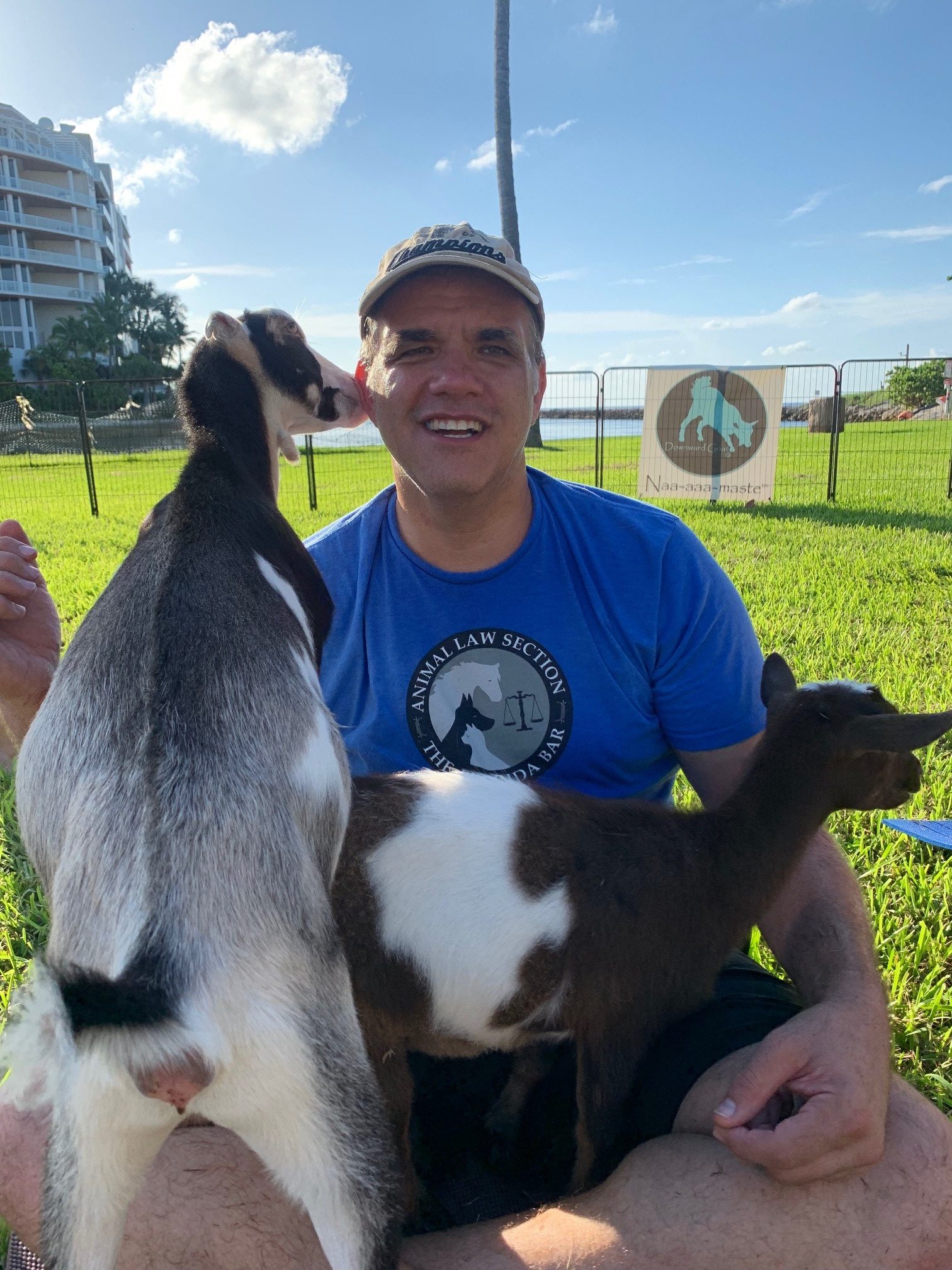 matt with two large goats, one in his lap and the other one biting his ear