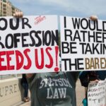 law students protesting in front of the supreme court with signs that says our profession needs us and I would rather be taking the bar exam