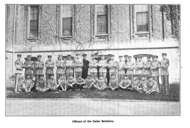 Black and white picture of boys, ages 10 to 18, in military dress in front of a building