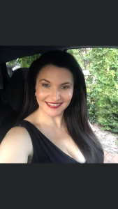 justine sitting in her car smiling wearing a black dress