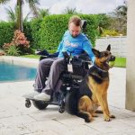 Jordan in his wheelchair with his dog outside on the patio next to a pool