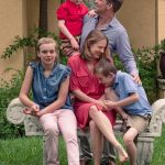 Jennifer stilling on a bench with two of her children and Blake standing behind her holding their third child