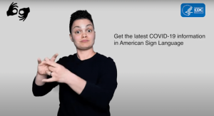 A person with short, black hair wearing a black shirt uses American Sign Language (ASL) to introduce the COVID-19 informational video series. They stand in front of a gray backdrop next to a text block that reads: Get the latest COVID-19 information in American Sign Language.