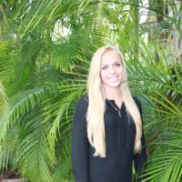 Alex standing in front of palm trees smiling and wearing a black dress Alex standing in front of palm trees smiling and wearing a black dress