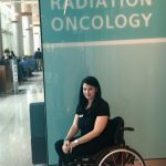 justine sitting in her wheelchair under a sign that says radiation oncology justine sitting in her wheelchair under a sign that says radiation oncology