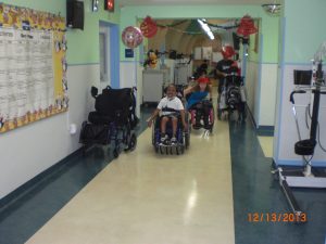 Stephanie and a young man racing wheelchairs down the hallaway