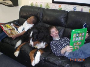 2 medically fragile boys reading books on a couch using a big dog as a pillow