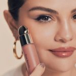 selena gomez holding a bottle of rare beauty make up next to her face