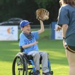 a young boy using a wheelchair playing baseball. he is wearing a glove and catching a ball