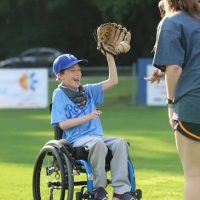 a young boy using a wheelchair playing baseball. he is wearing a glove and catching a ball a young boy using a wheelchair playing baseball. he is wearing a glove and catching a ball